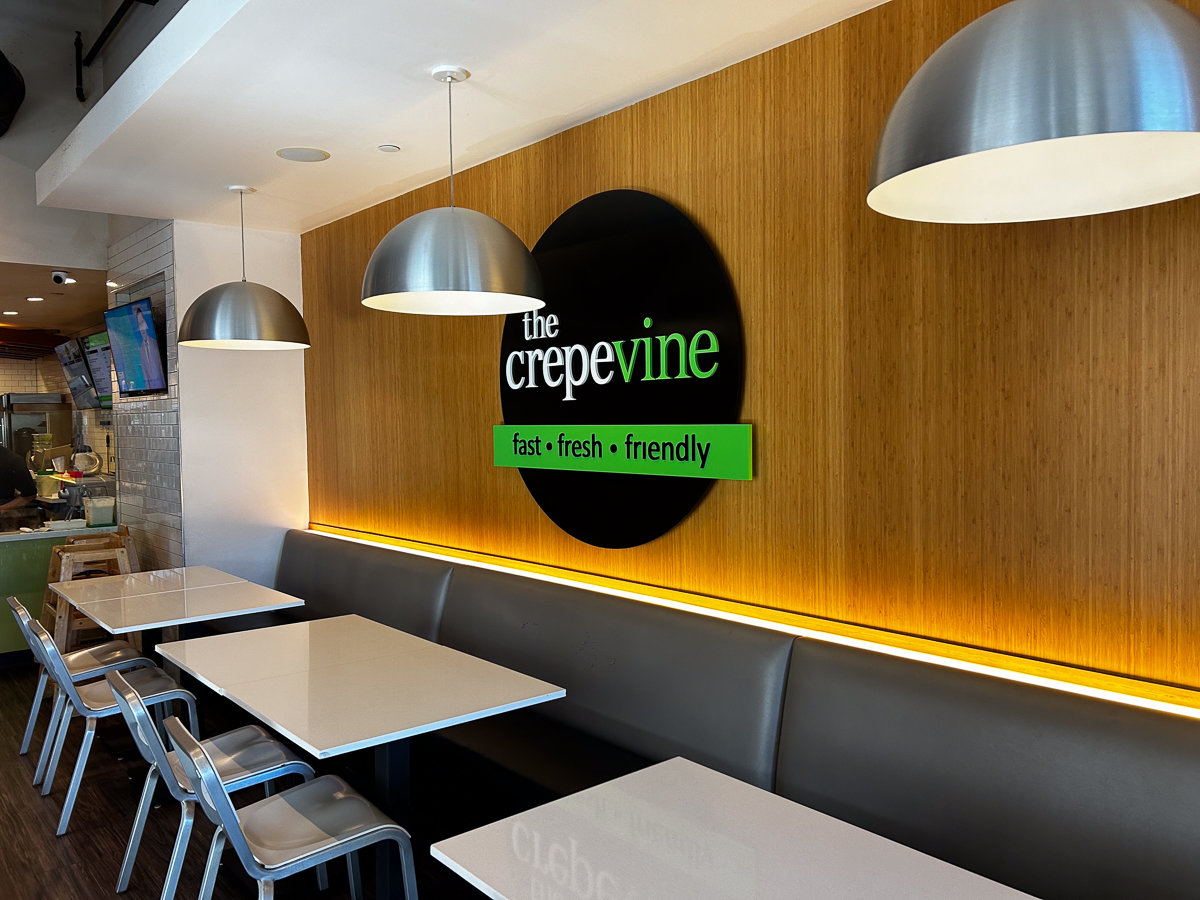 inside crepevine with metal tables and black and green circle sign